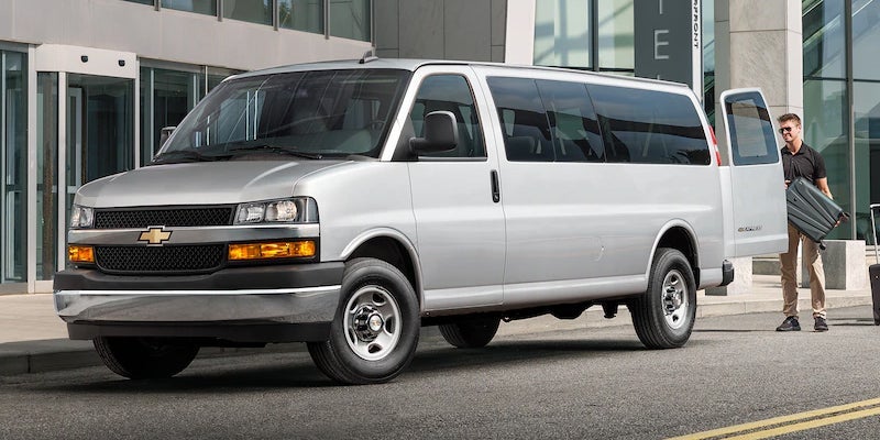 Silver Chevrolet Express passenger van parked in an urban setting with a side passenger door open