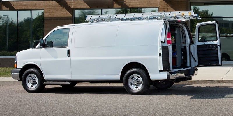White Chevrolet Express cargo van parked outside a commercial building, featuring a roof-mounted ladder rack