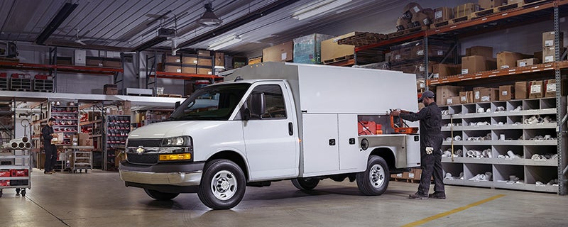 White Chevrolet Express service utility van parked inside a warehouse, featuring side-mounted tool compartments