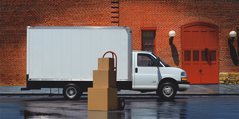 White Chevrolet Express box truck parked near a loading area, featuring a large enclosed cargo box designed for commercial deliveries
