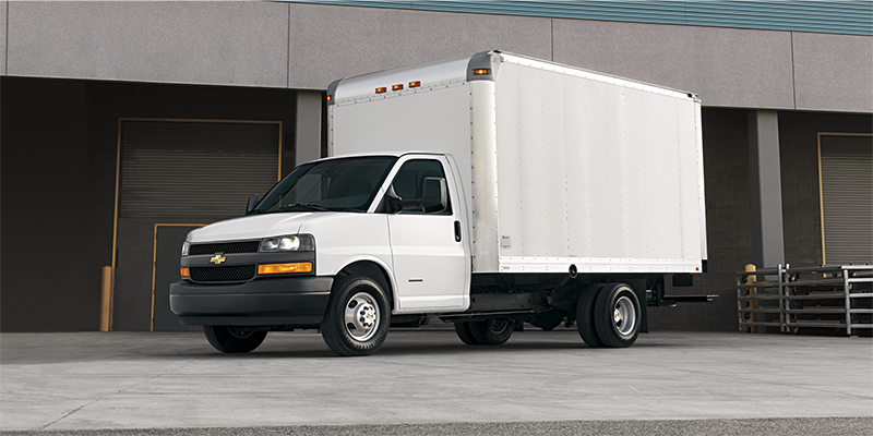 White Chevrolet Express commercial cube van parked outside an industrial building