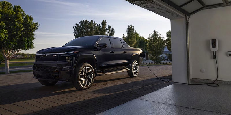 Chevrolet Silverado EV pickup truck parked in a residential driveway and connected to a wall-mounted home charging station