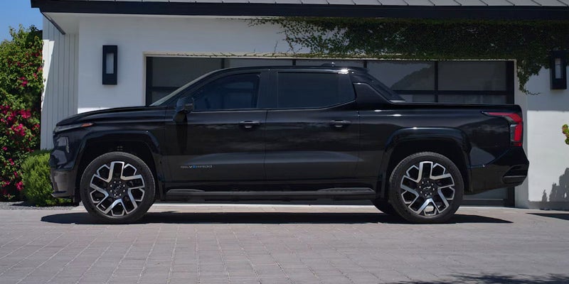 Side profile of a black Chevrolet Silverado EV parked in front of a modern home