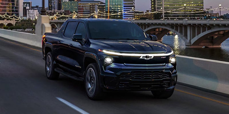 Chevrolet Silverado EV traveling across a city bridge at night with illuminated buildings and urban scenery in the background