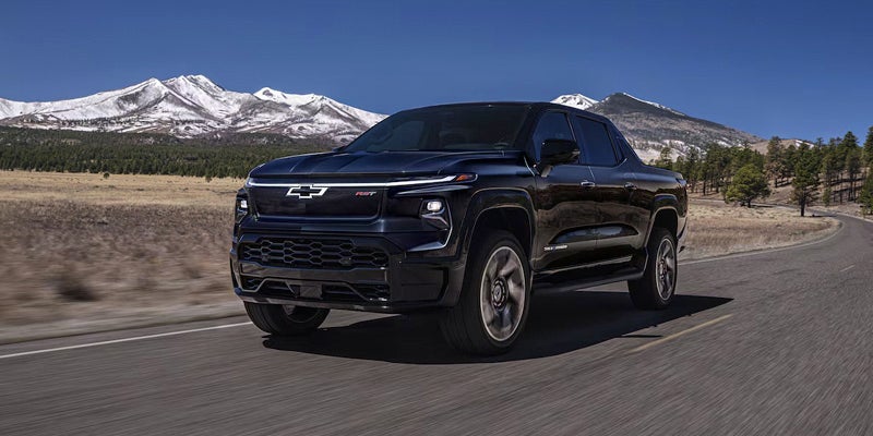 Chevrolet Silverado EV driving on an open highway with snow-capped mountains and a clear blue sky in the background