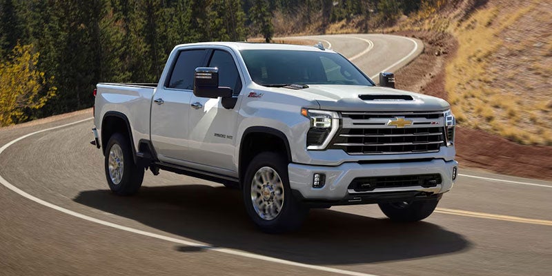 White Chevrolet Silverado HD pickup truck driving on a winding mountain road, featuring a chrome grille