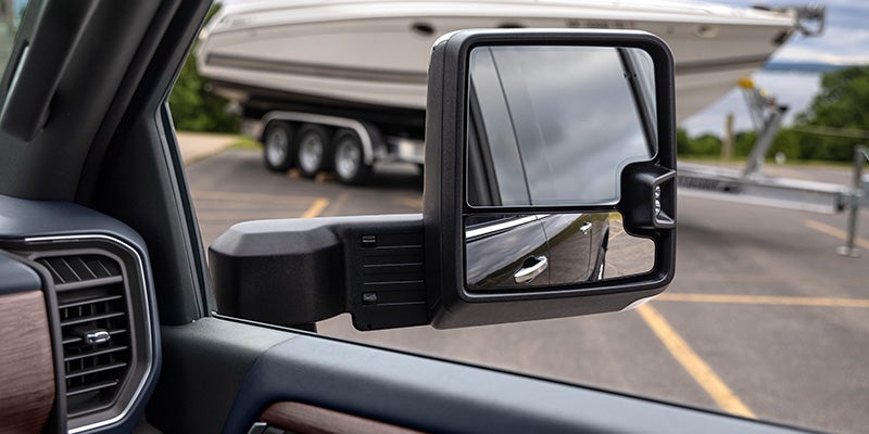 Close-up of a Chevrolet Silverado HD towing mirror reflecting a boat trailer parked behind the truck