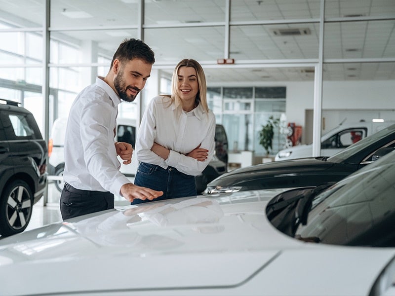 Man showing a smiling woman a white car in a dealership showroom