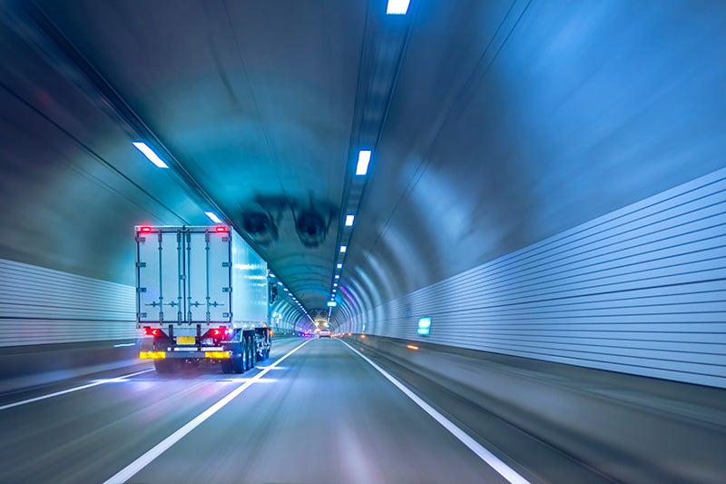 White truck drives through a long, blue-lit tunnel with distinct road markings
