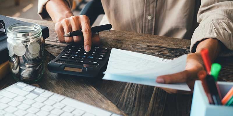 Close-up of a person using a calculator while reviewing financial documents at a wooden desk