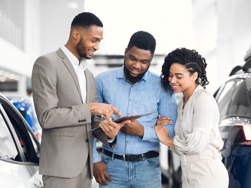 Car salesman showing a smiling couple details on a clipboard in a car dealership