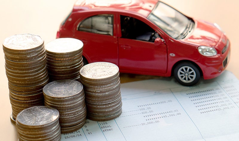 Red toy car, stacks of coins, and a financial ledger, symbolizing car expenses, savings, or loans.
